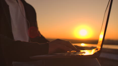 Gewölbeplan-Einer-Hand,-Die-Bei-Sonnenuntergang-Auf-Einer-Laptoptastatur-Tippt,-Mit-Blick-Auf-Die-Stadt-Aus-Der-Höhe.-Programmierer-Arbeitet-Auf-Dem-Dach-Eines-Gebäudes.